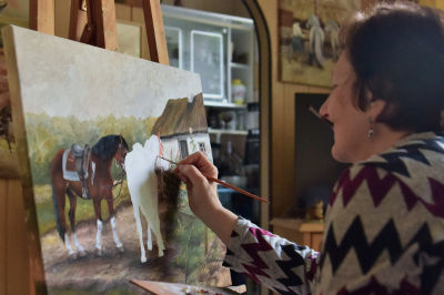 Urszula Chromik maluje obraz. Na obrazie konie. 