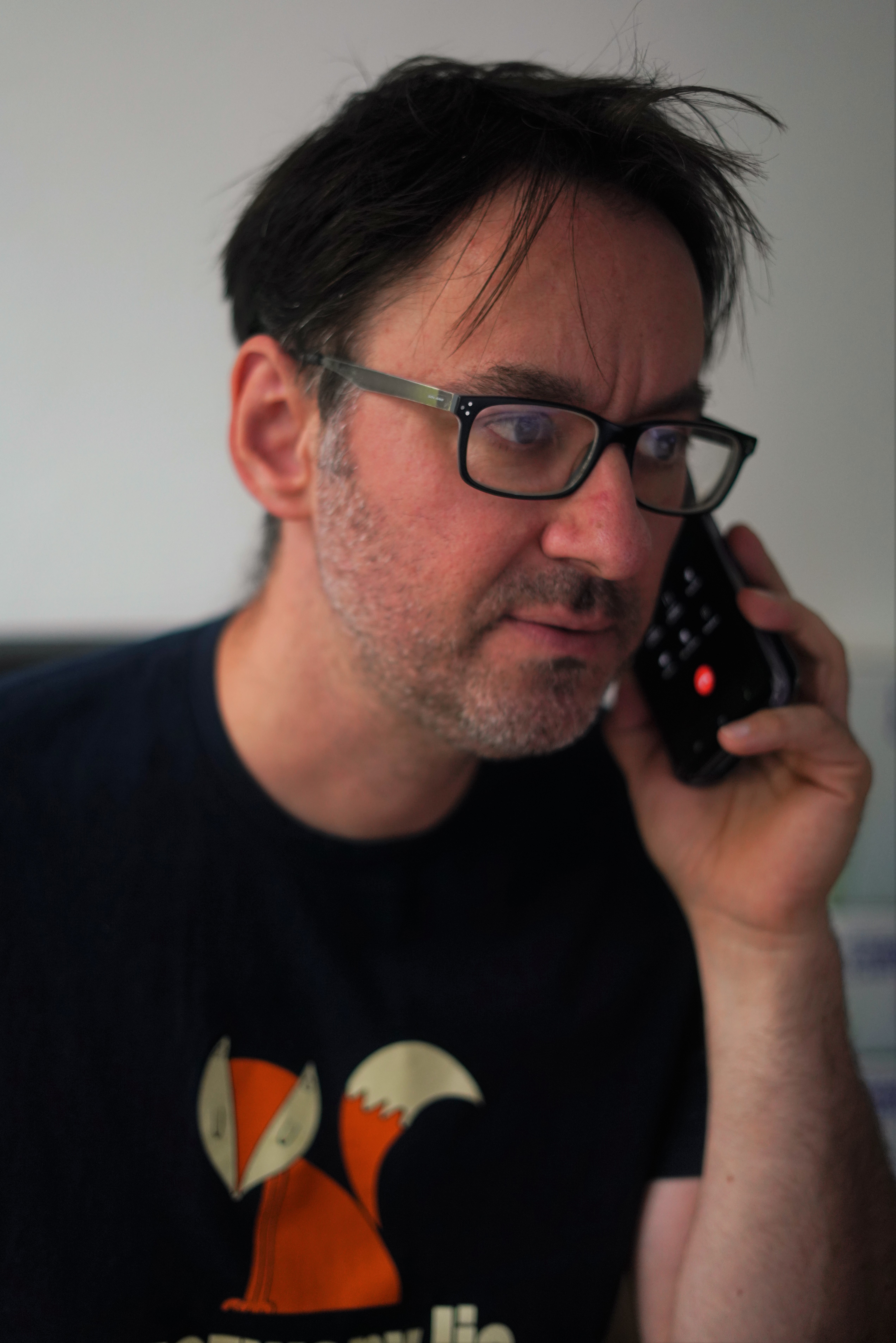 Maciej Lisak. Trzyma przy uchu telefon. Ubrany w koszulkę z rysunkiem rudego lisa.